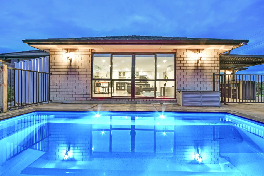 Swimming pool lit at dusk behind a modern home