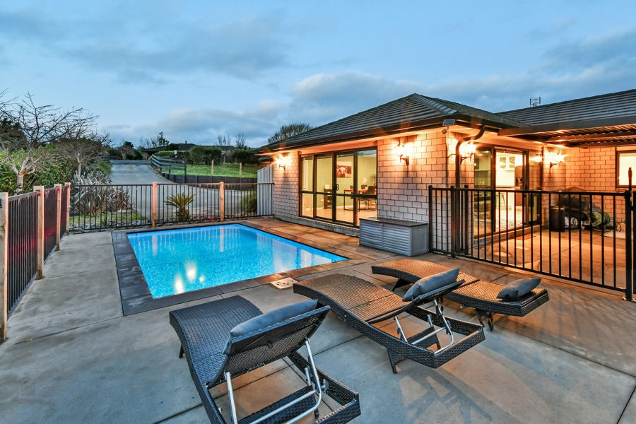 Finished pool and paved surrounds beside a home at dusk